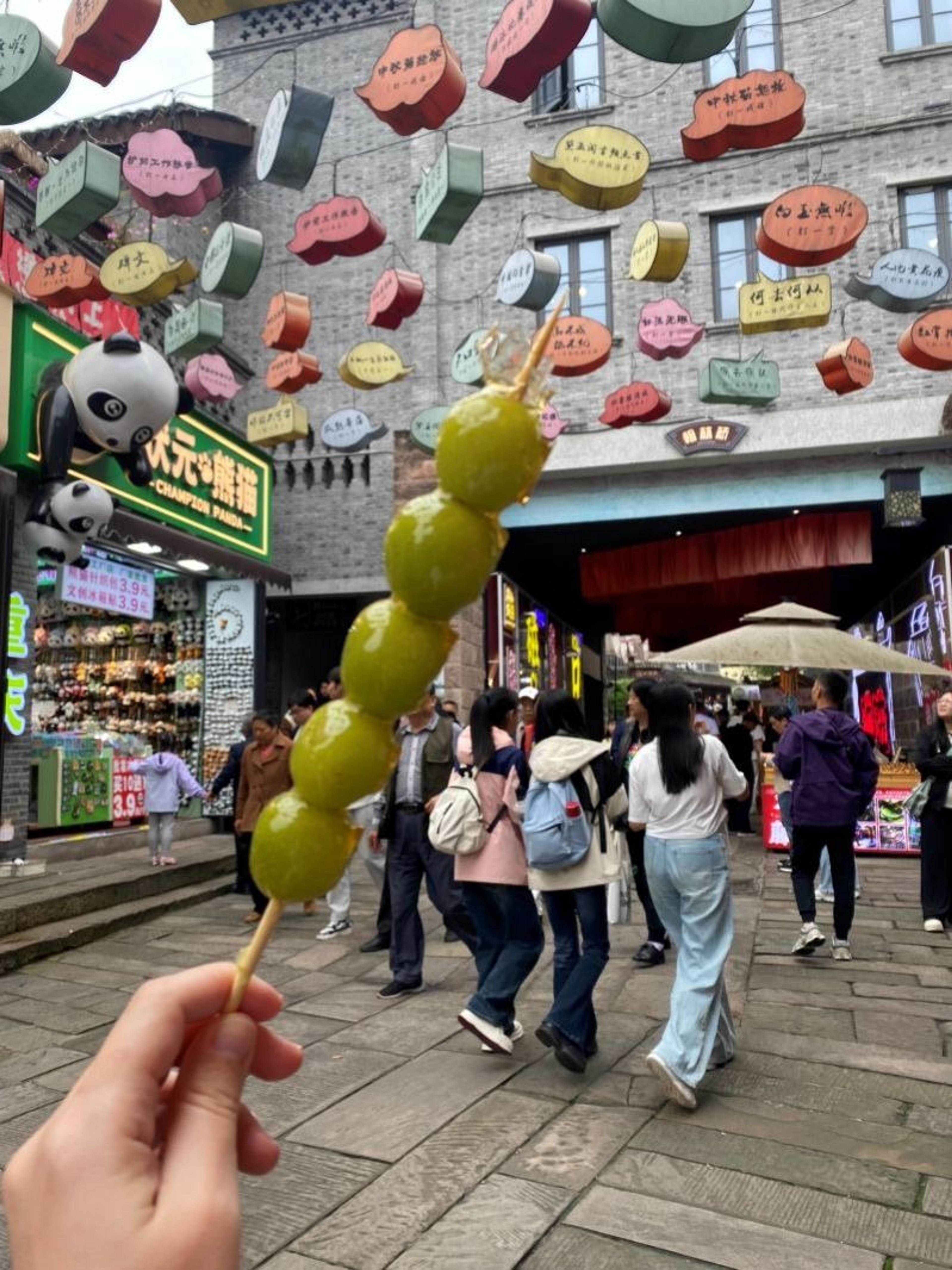Outdoor shopping area in Chengdu, China, featuring a colorful display, lively crowd, and sugared fruit skewers.