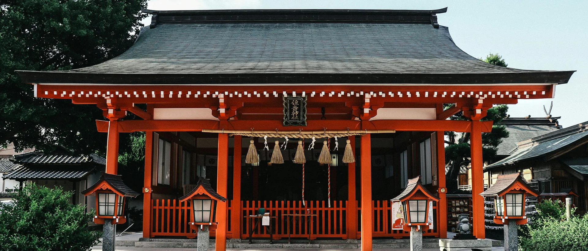 A vibrant red Shinto shrine stands prominently in Kyoto, Japan, adorned with traditional lanterns and sacred ropes.