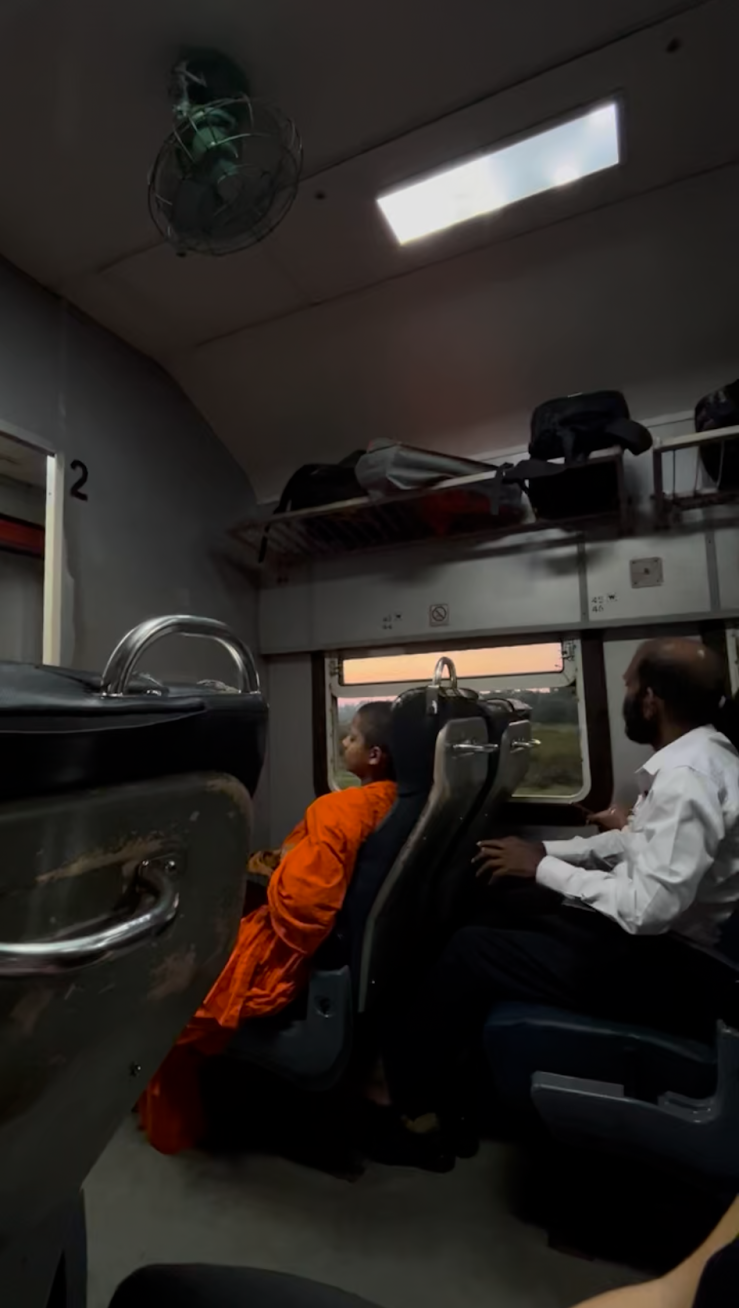 Passengers relax in seats of a train cabin in Sri Lanka, as the evening sky is visible through the window.