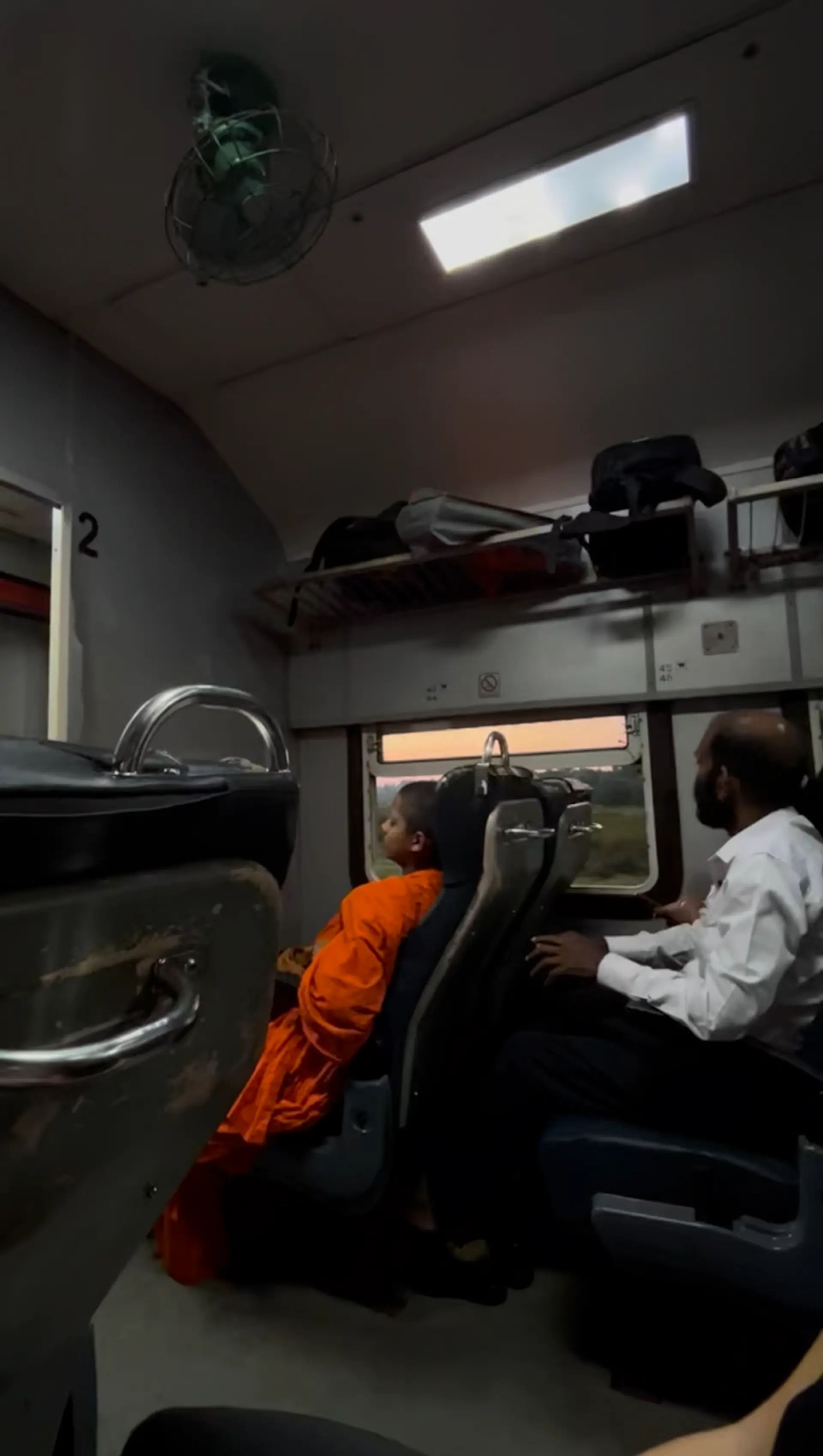 Passengers relax in seats of a train cabin in Sri Lanka, as the evening sky is visible through the window.