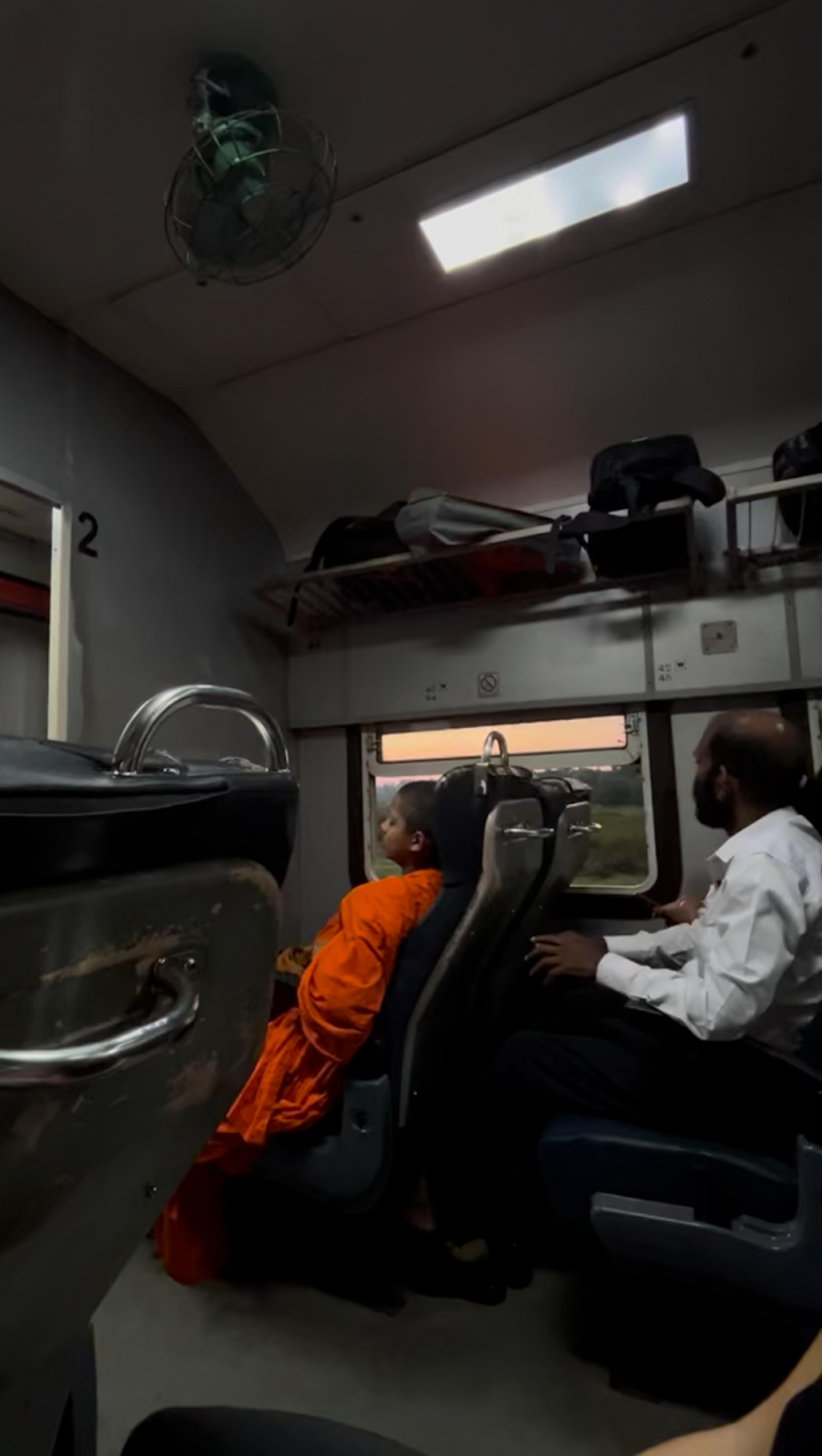 Passengers relax in seats of a train cabin in Sri Lanka, as the evening sky is visible through the window.