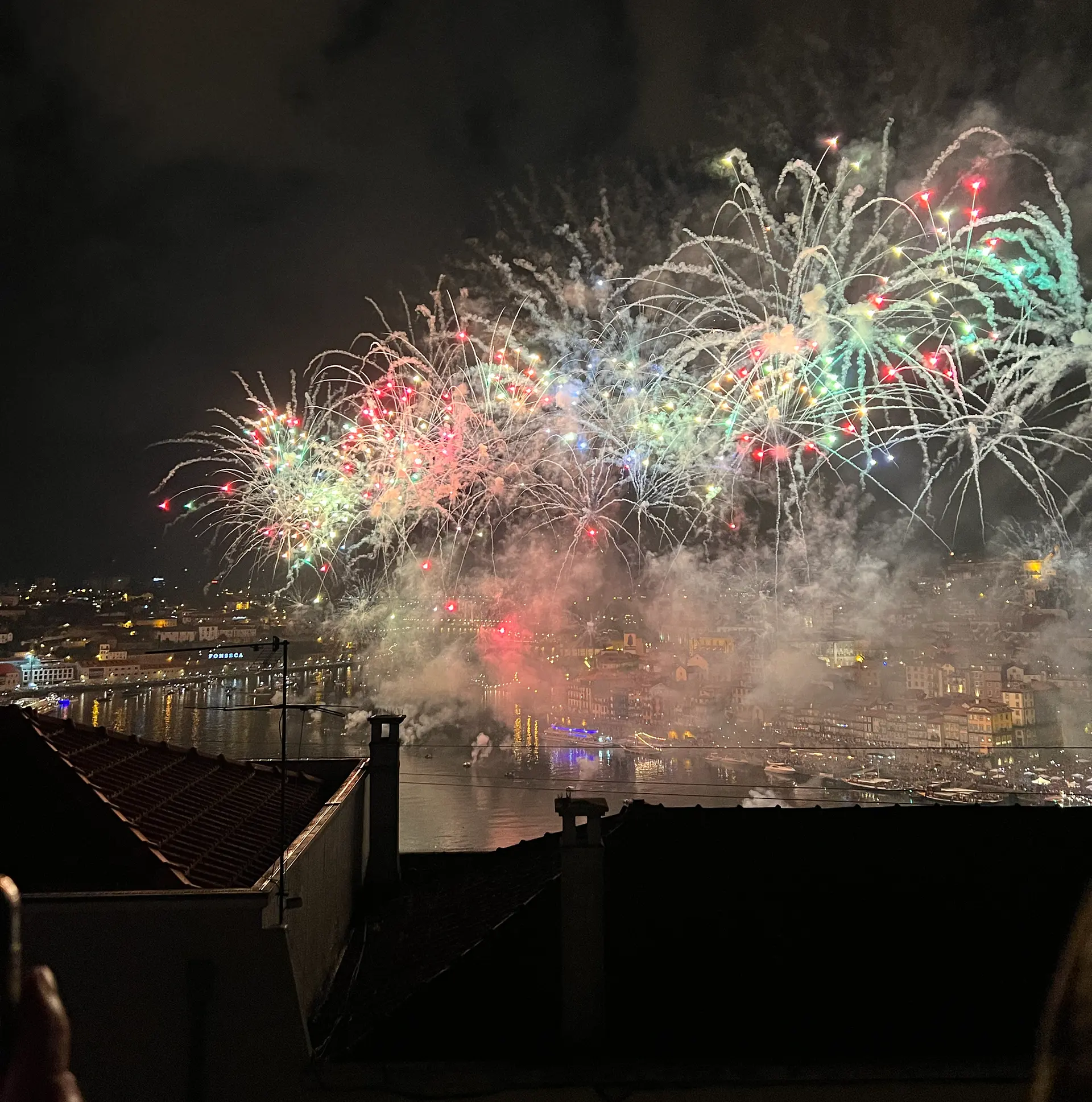 Colorful fireworks light up the night sky above Porto's waterfront, reflecting over the Douro River during the Sao Joao festival.