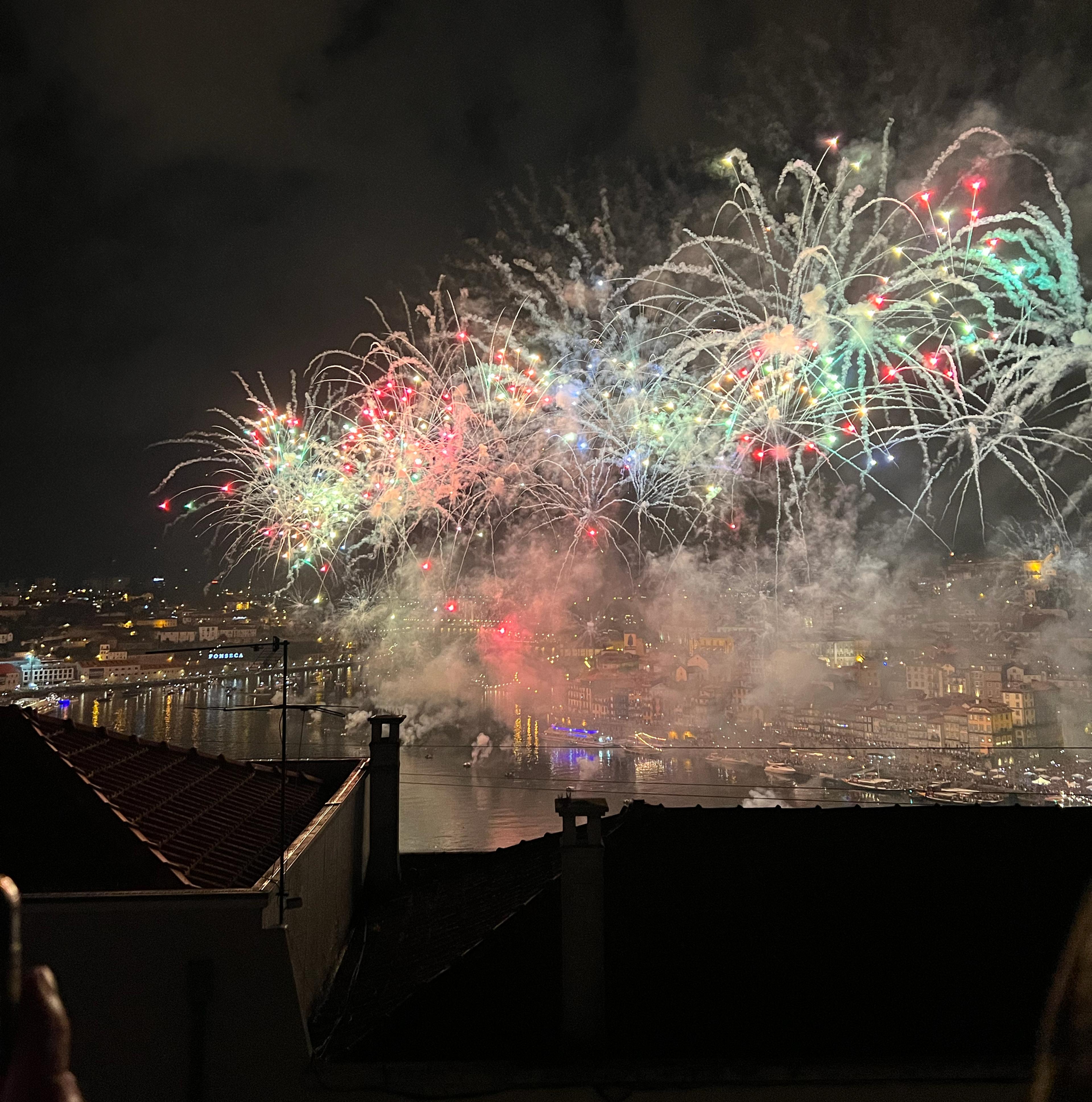 Colorful fireworks light up the night sky above Porto's waterfront, reflecting over the Douro River during the Sao Joao festival.