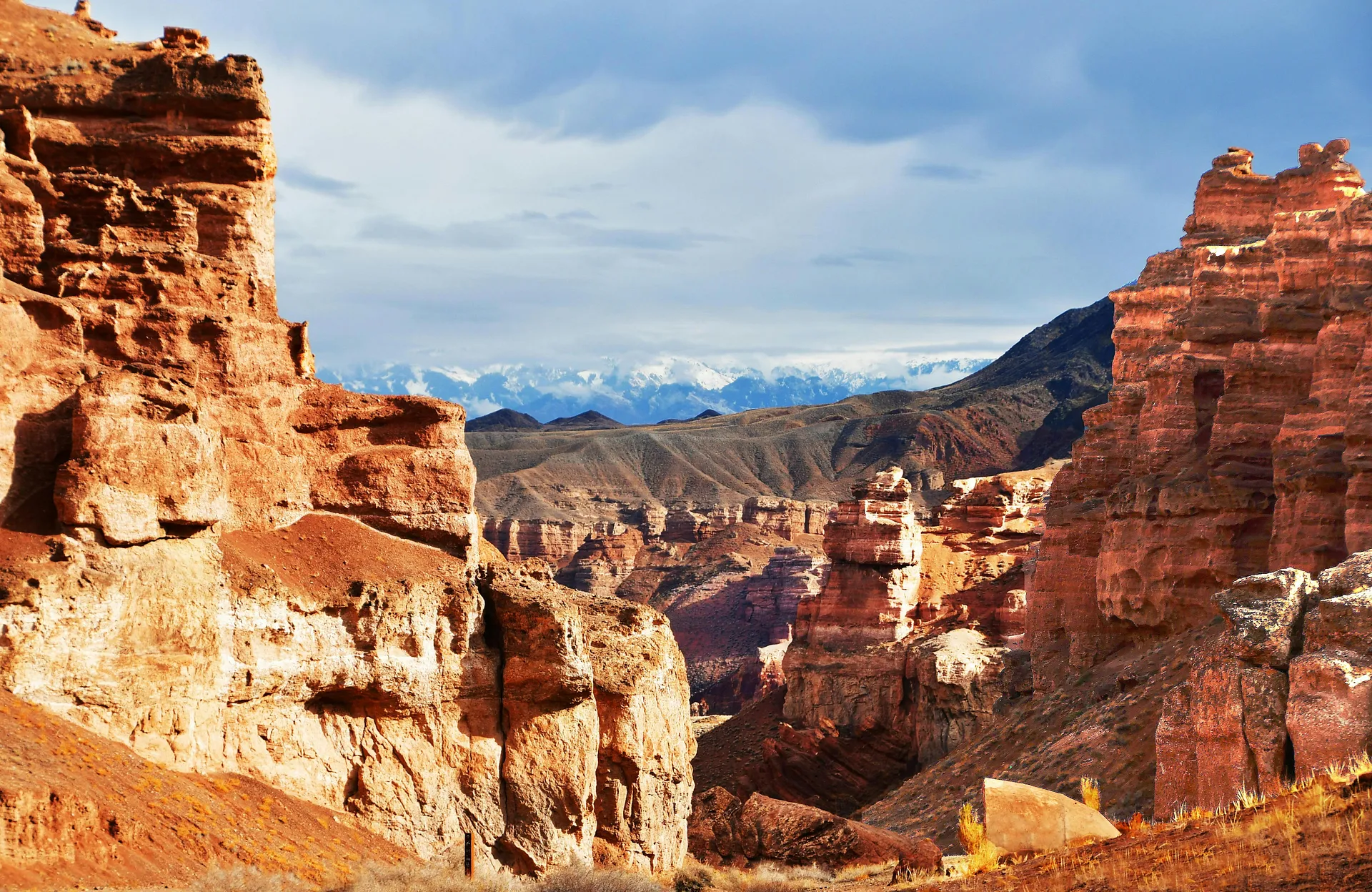 The stunning red rock formations of Charyn Canyon in Kazakhstan create a dramatic landscape against a backdrop of distant snow-capped mountains.