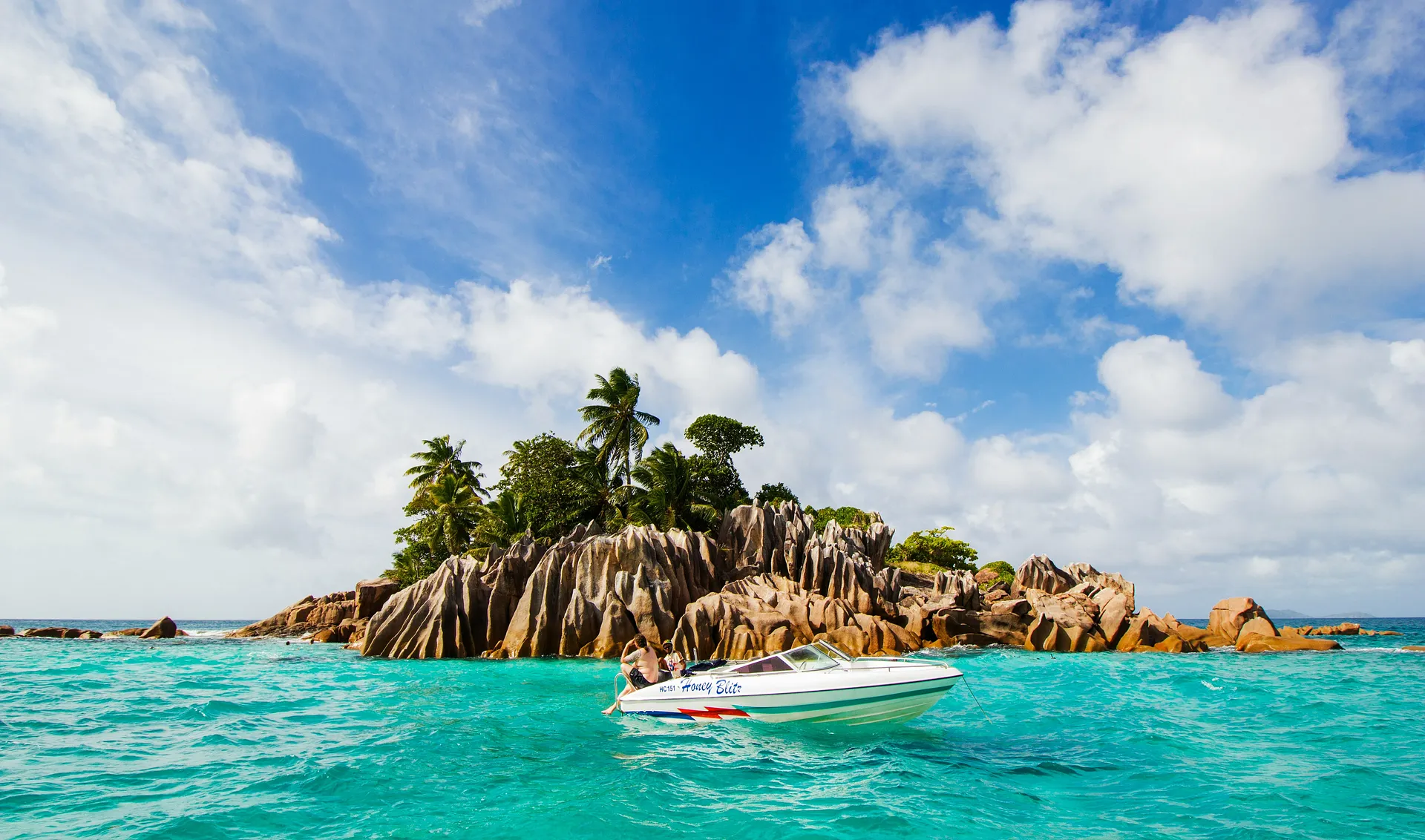 A small speedboat floats beside the iconic granite boulders and turquoise waters of La Digue in the Seychelles.