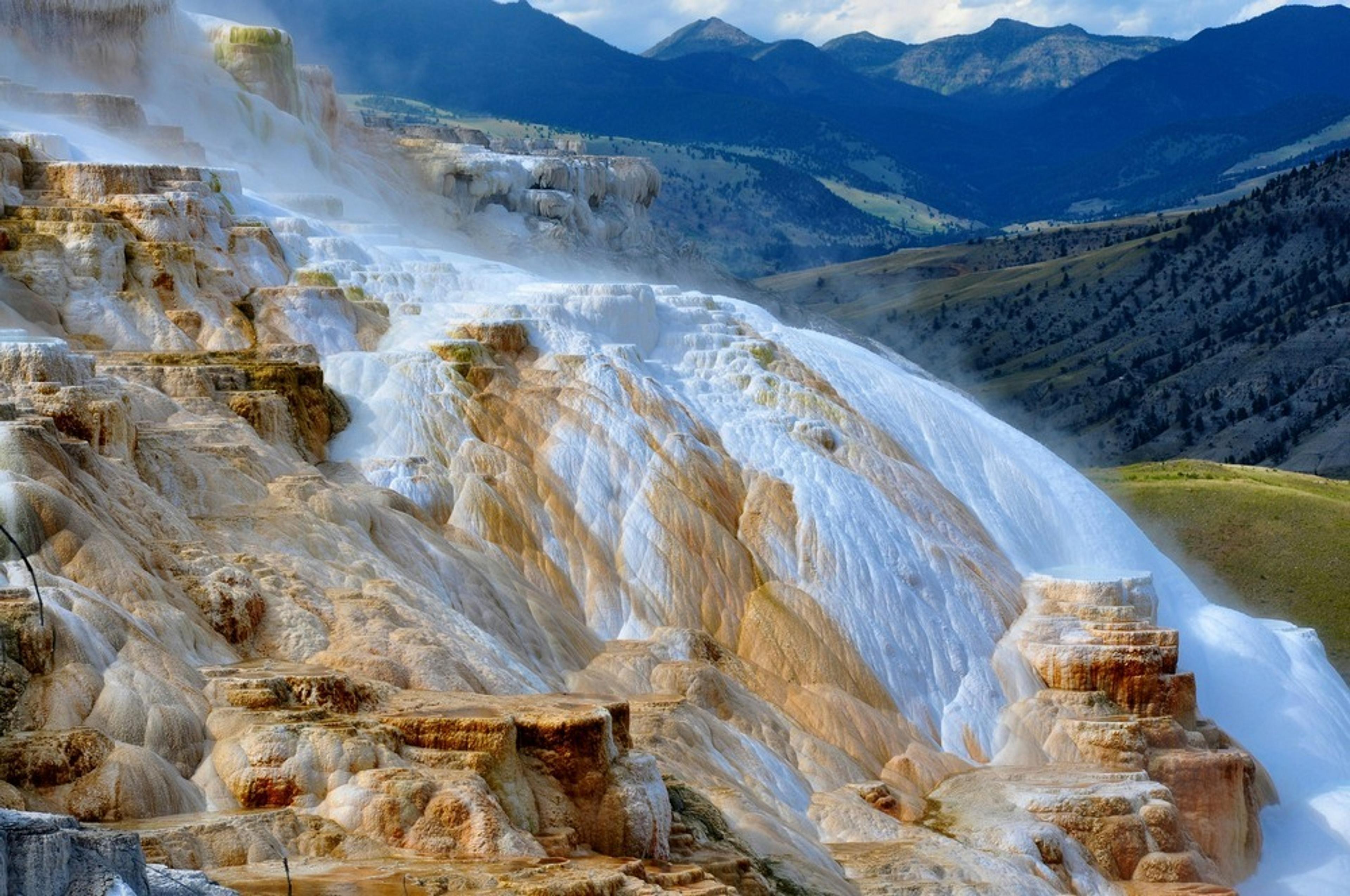Terraced travertine formations at Mammoth Hot Springs in Yellowstone National Park against a backdrop of distant mountains.
