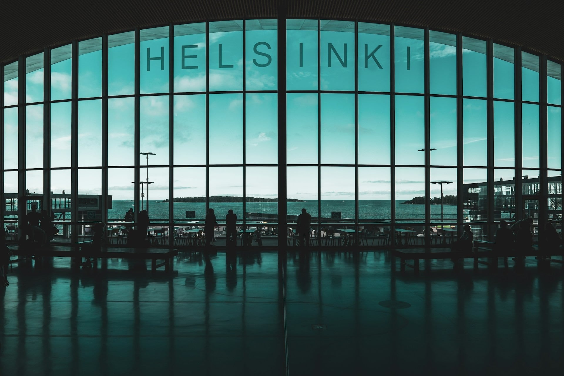 Large glass windows overlooking the sea in Helsinki, Finland, with silhouetted figures inside.