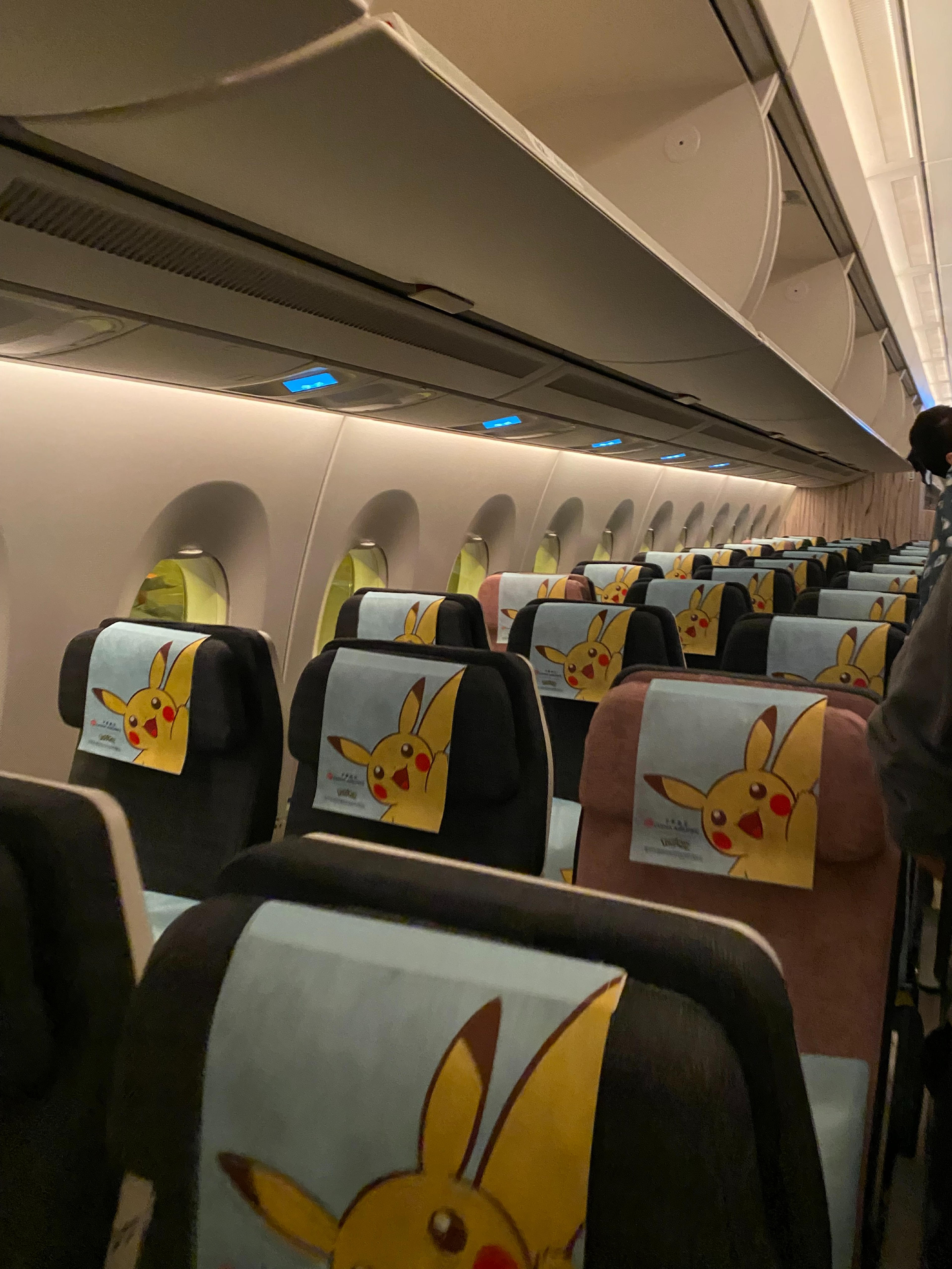The interior of a Pokémon-themed airplane cabin with Pikachu headrest covers exudes a playful atmosphere.