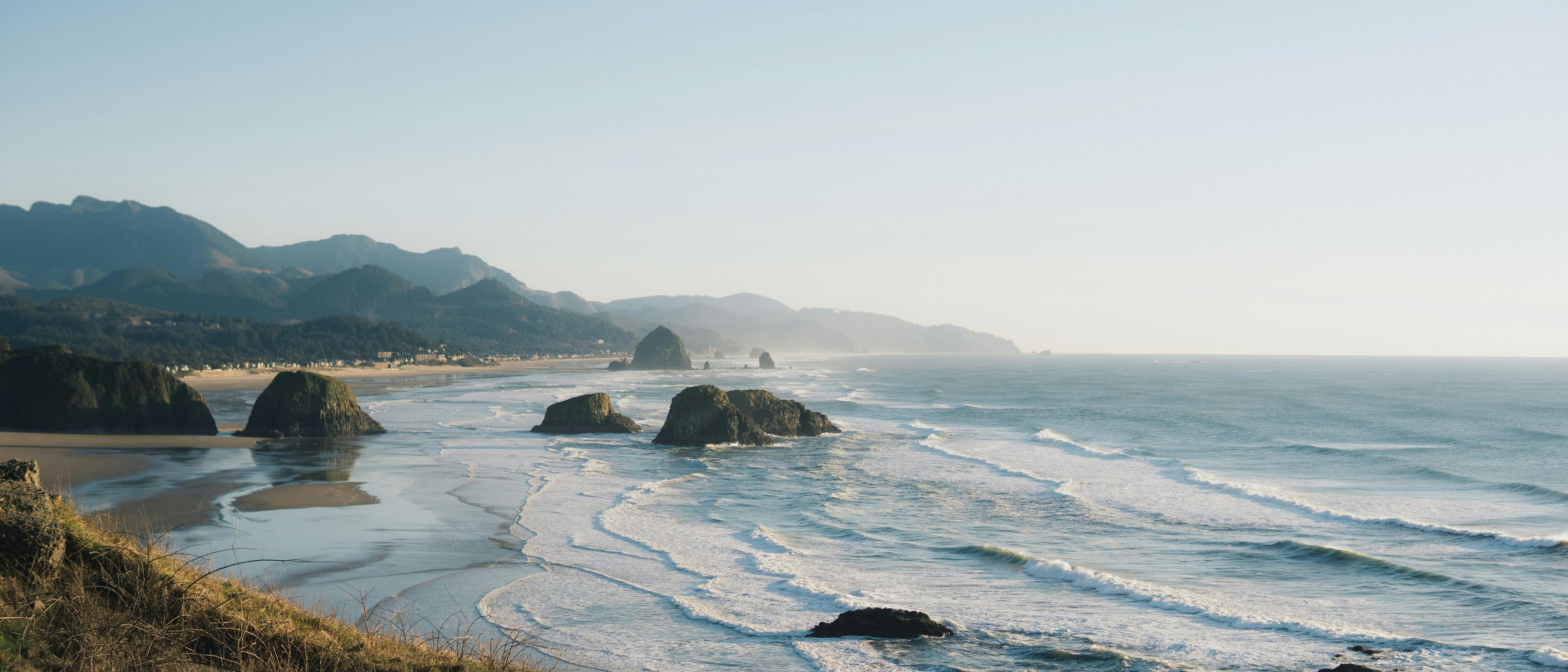 Coastal waves gently break along the shores of Cannon Beach in Oregon, with the iconic Haystack Rock in the distance.